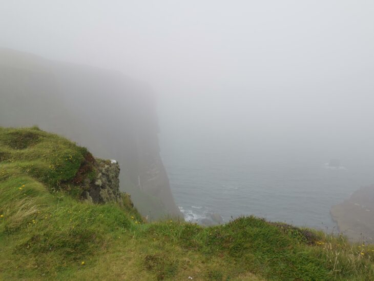 A steep sea cliff shrouded in dense mist.