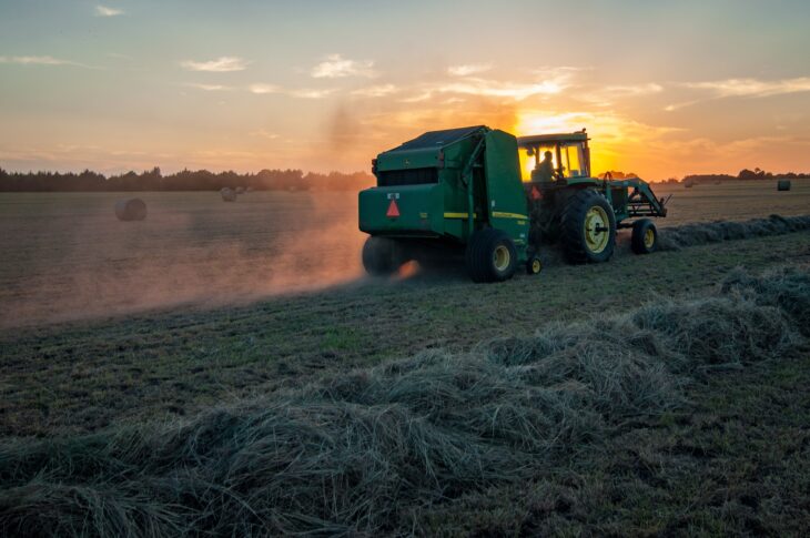 Straw being baled with a bailer and tractor at sunset