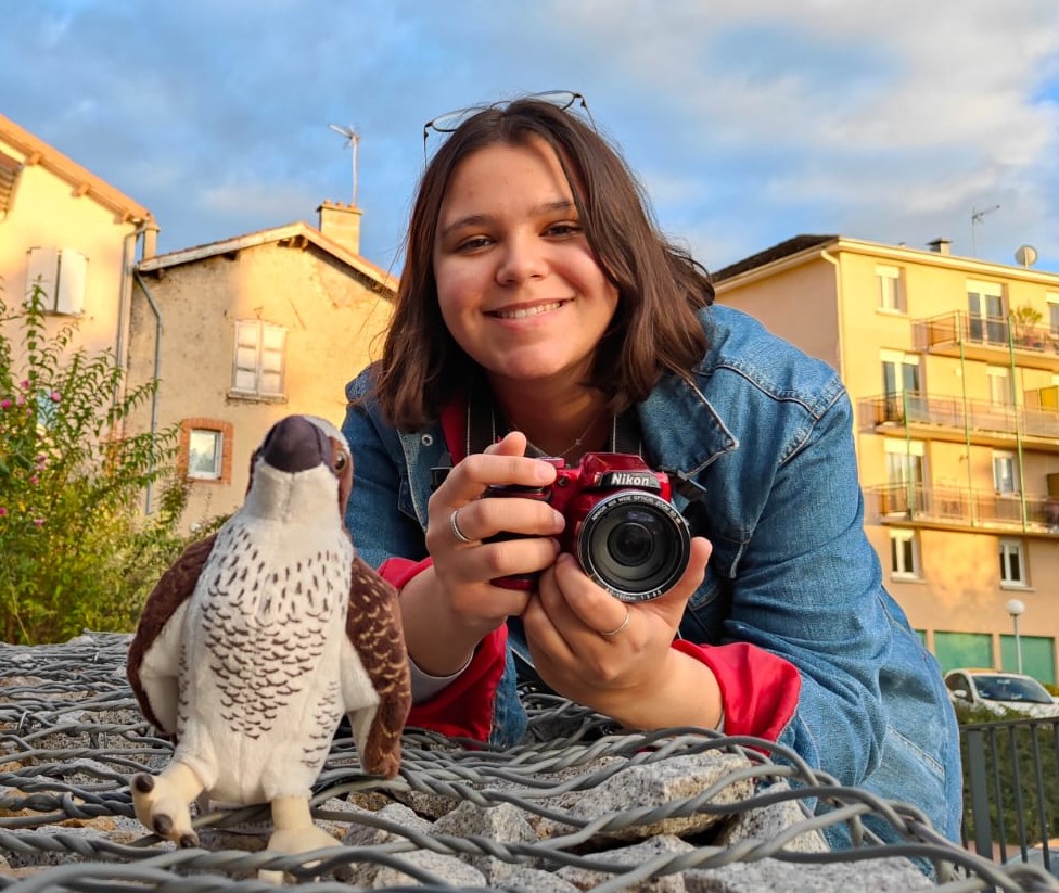 A person holding a camera next to an osprey soft toy.