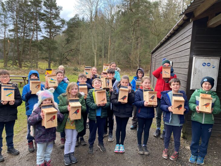 A group of children from the Perth Wildlife Watch holding up bird boxes that they have painted.